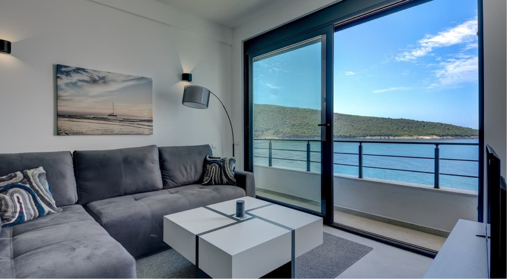 Wohnzimmer einer Ferienwohnung in Montenegro mit grauem Ecksofa, Balkon und direktem Meerblick